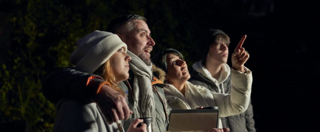 Family looking up to the night sky while mother points