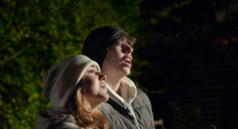 Sister and brother looking to sky while holding a book and hot drink