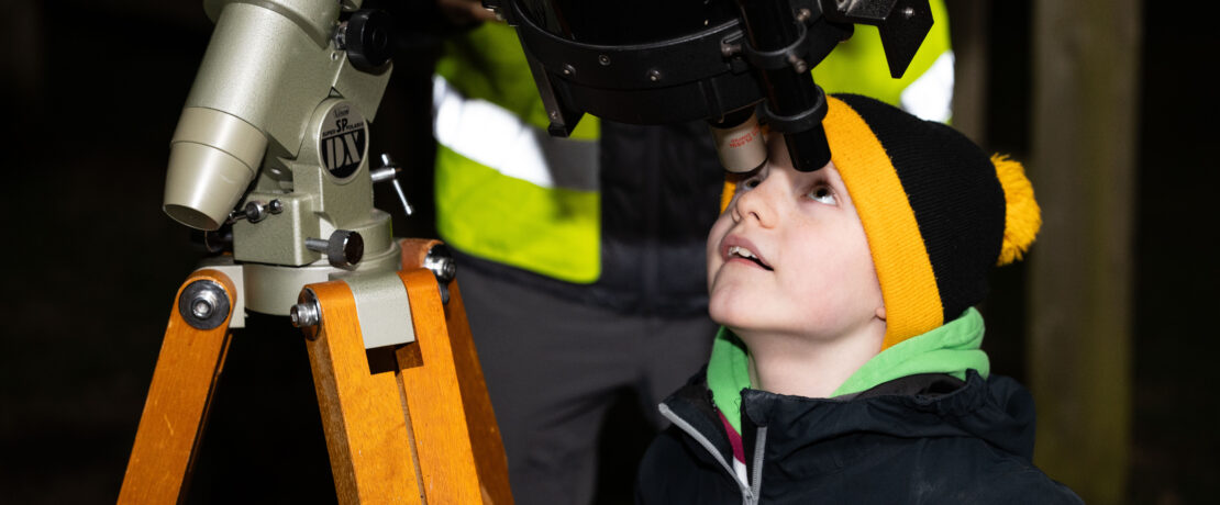 A boy in a woolly hat looking through a telescope