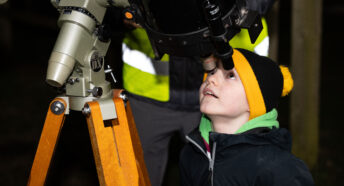 A boy in a woolly hat looking through a telescope