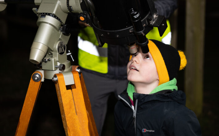 A boy in a woolly hat looking through a telescope