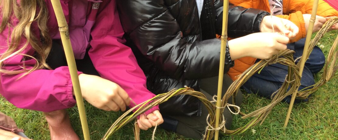 Three children crouching down and weaving willow