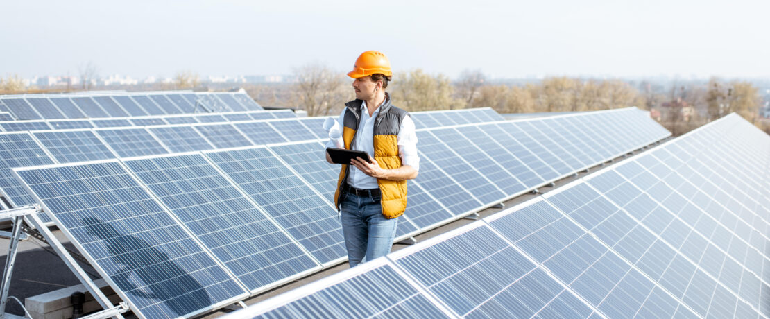 View on the rooftop solar power plant with mann walking and examining photovoltaic panels.